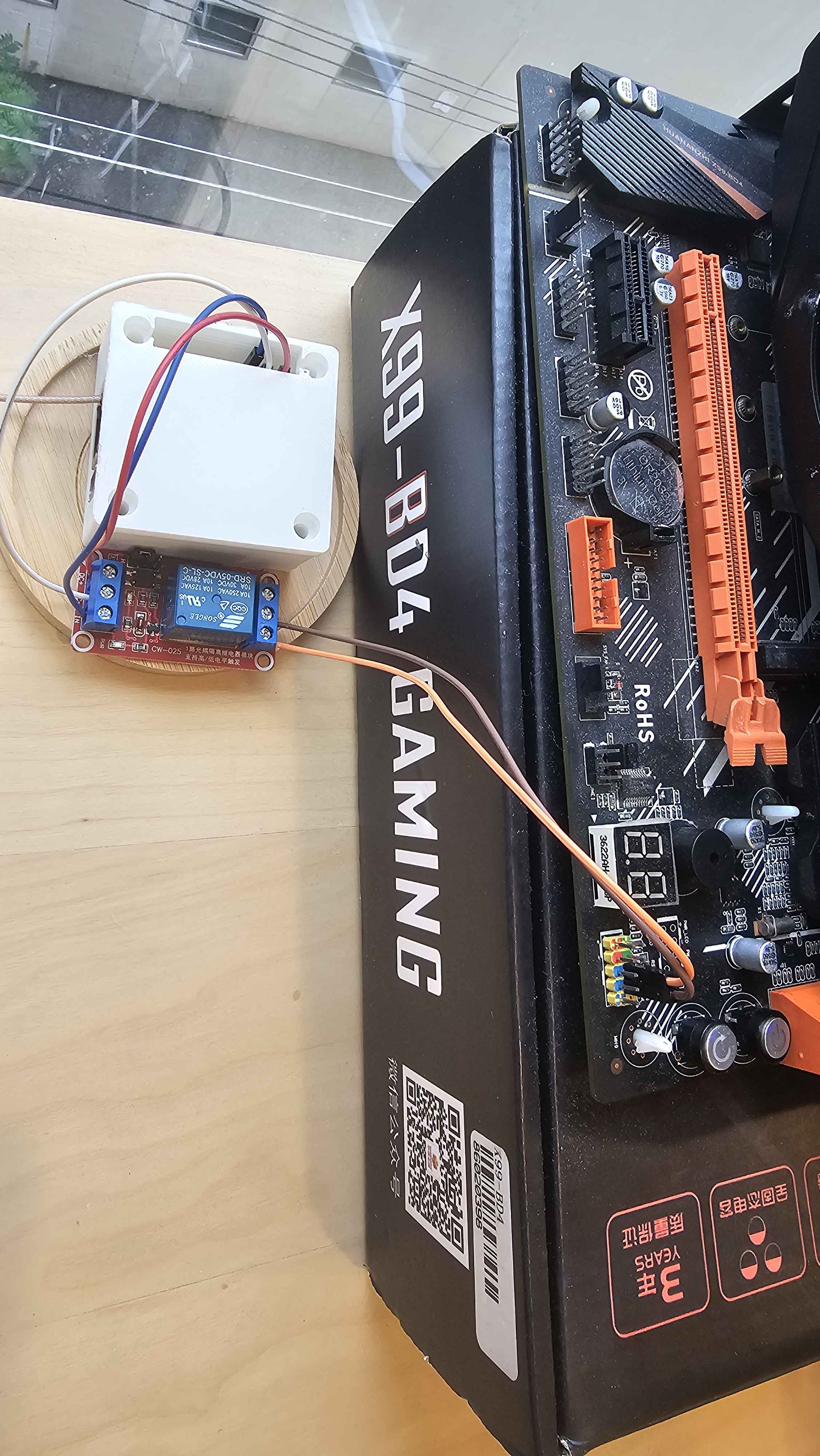 Relay module wired to the front panel power switch header on the Huananzhi X99 BD4, next to a 3D-printed enclosure